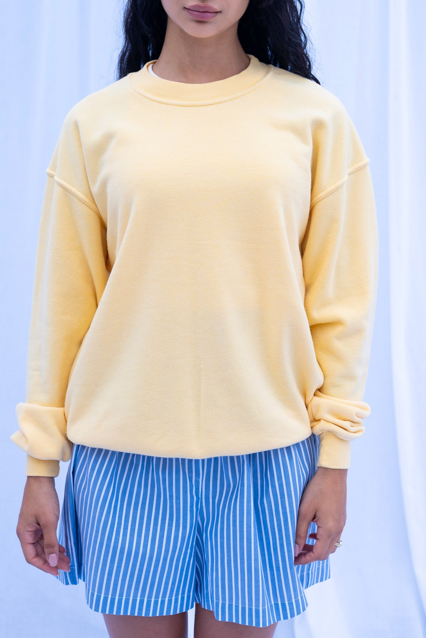Person wearing a light yellow sweatshirt and blue striped shorts against a white background