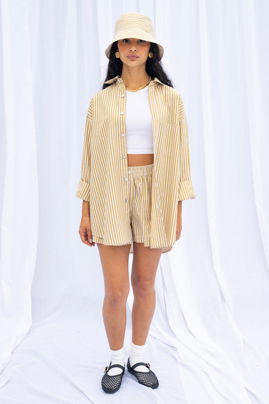 Person wearing a beige striped shirt, white top, shorts, and black shoes on a white background