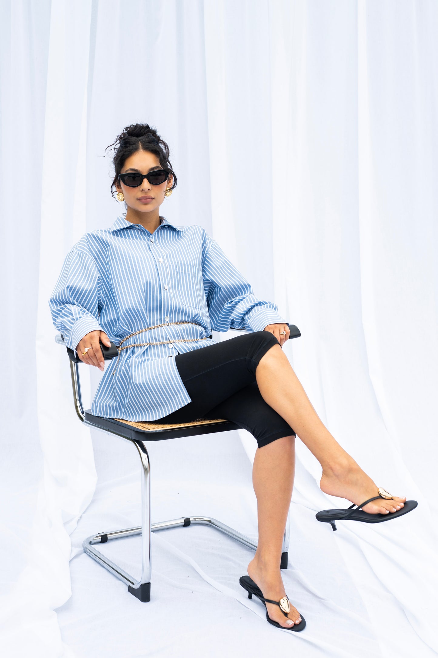 Woman sitting on a chair wearing a blue striped shirt and black skirt against a white background