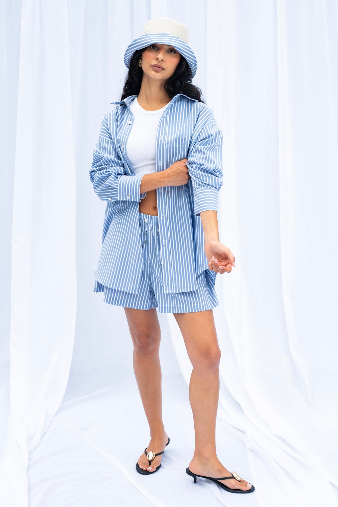 Woman wearing a blue and white striped shirt over a white dress with a matching hat on a white background