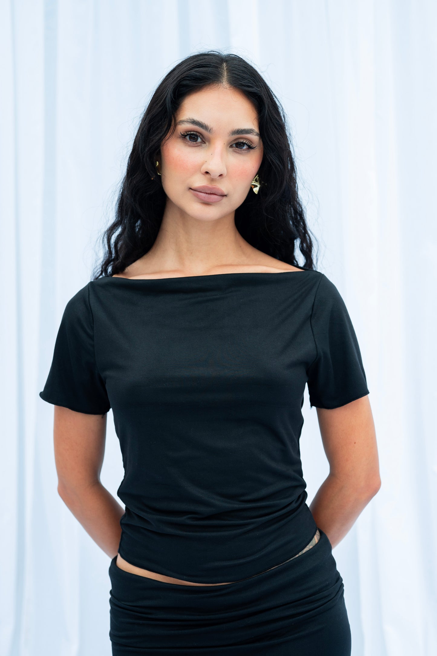 Woman wearing a black top and skirt against a white curtain background
