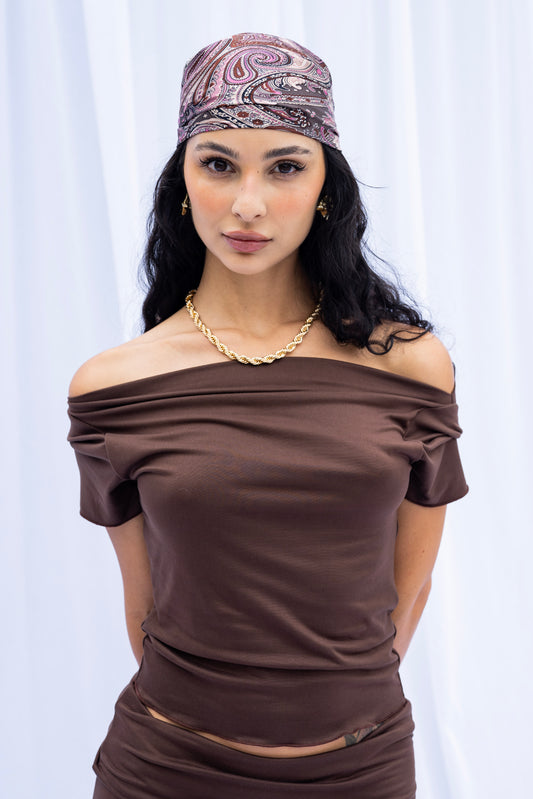 Woman wearing a brown off-shoulder top and headscarf against a white background