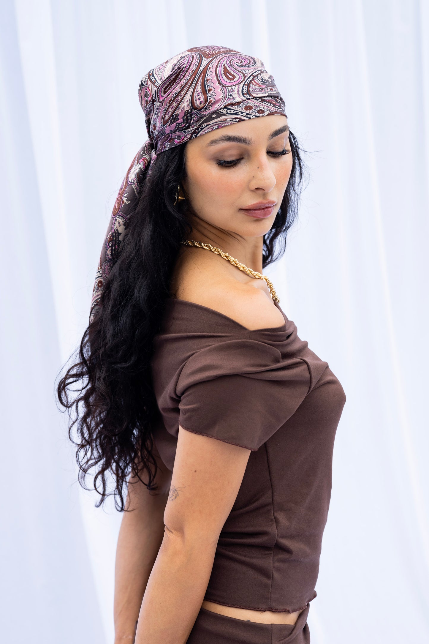 Woman wearing a patterned headscarf and brown top against a white background