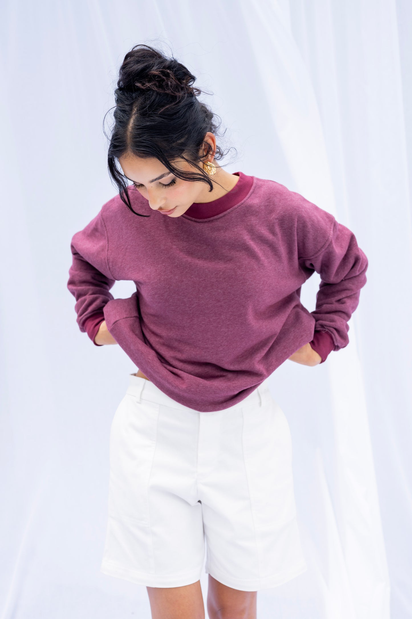 Woman wearing a mauve sweater and white shorts against a white background