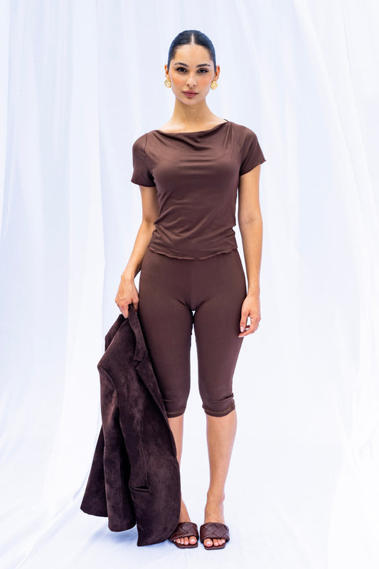 Woman wearing a brown outfit holding a matching jacket against a white background