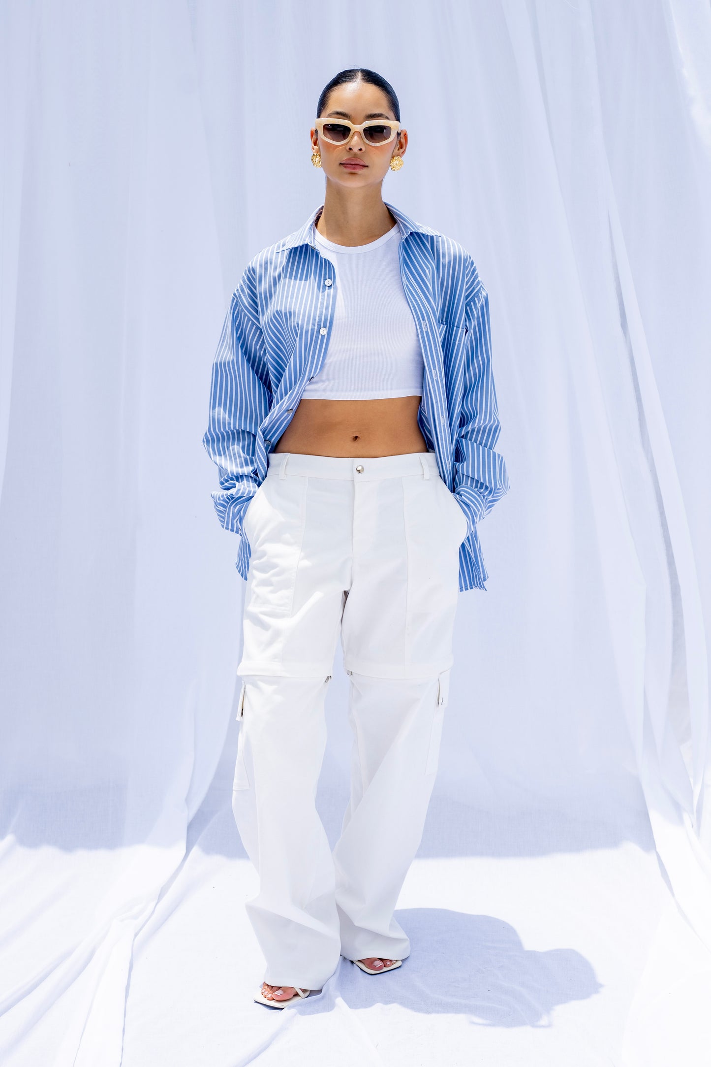 Person wearing a blue and white checkered shirt, white pants, and sunglasses on a white background
