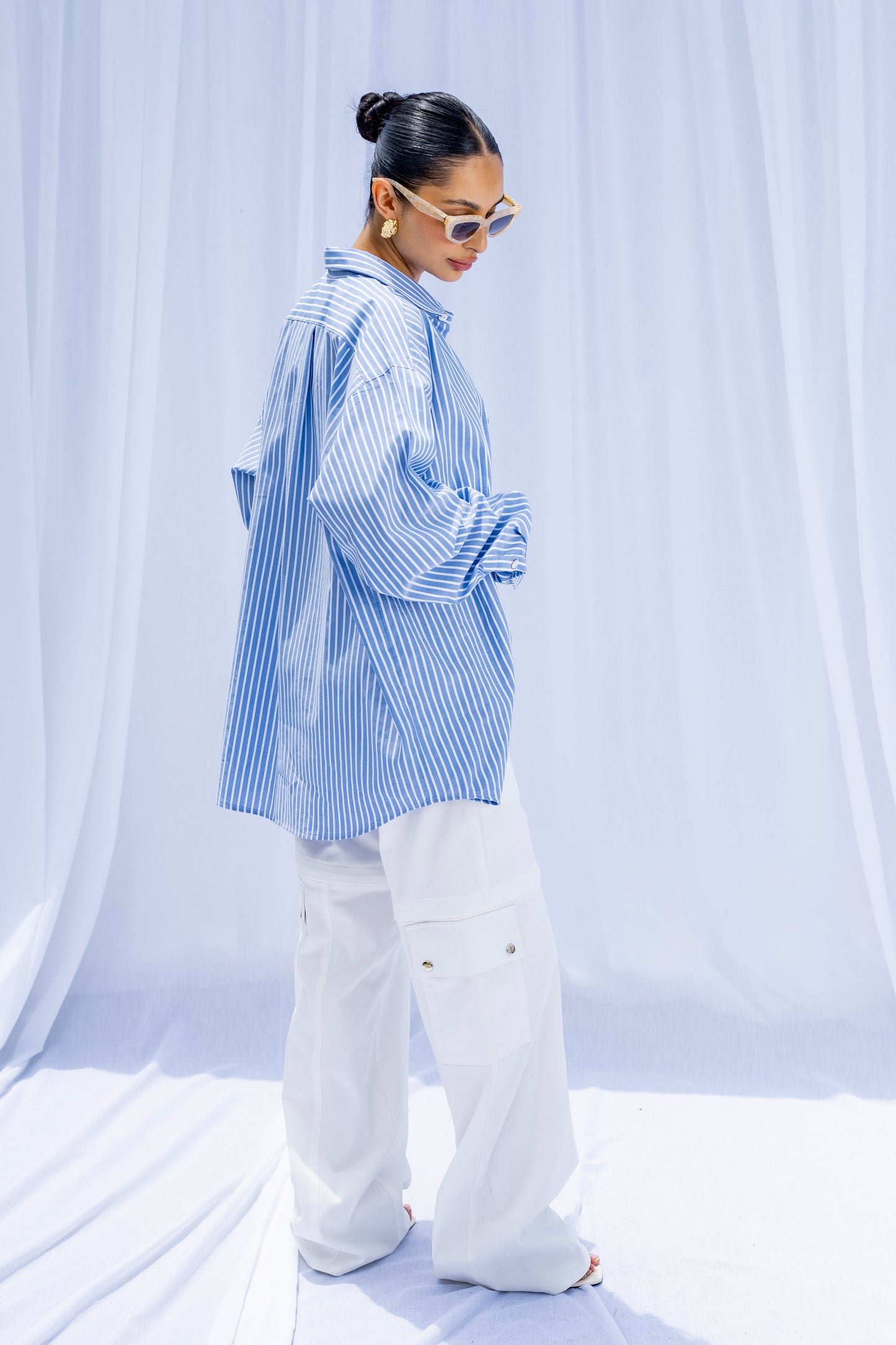 Person wearing a blue and white striped shirt with white pants against a white curtain background