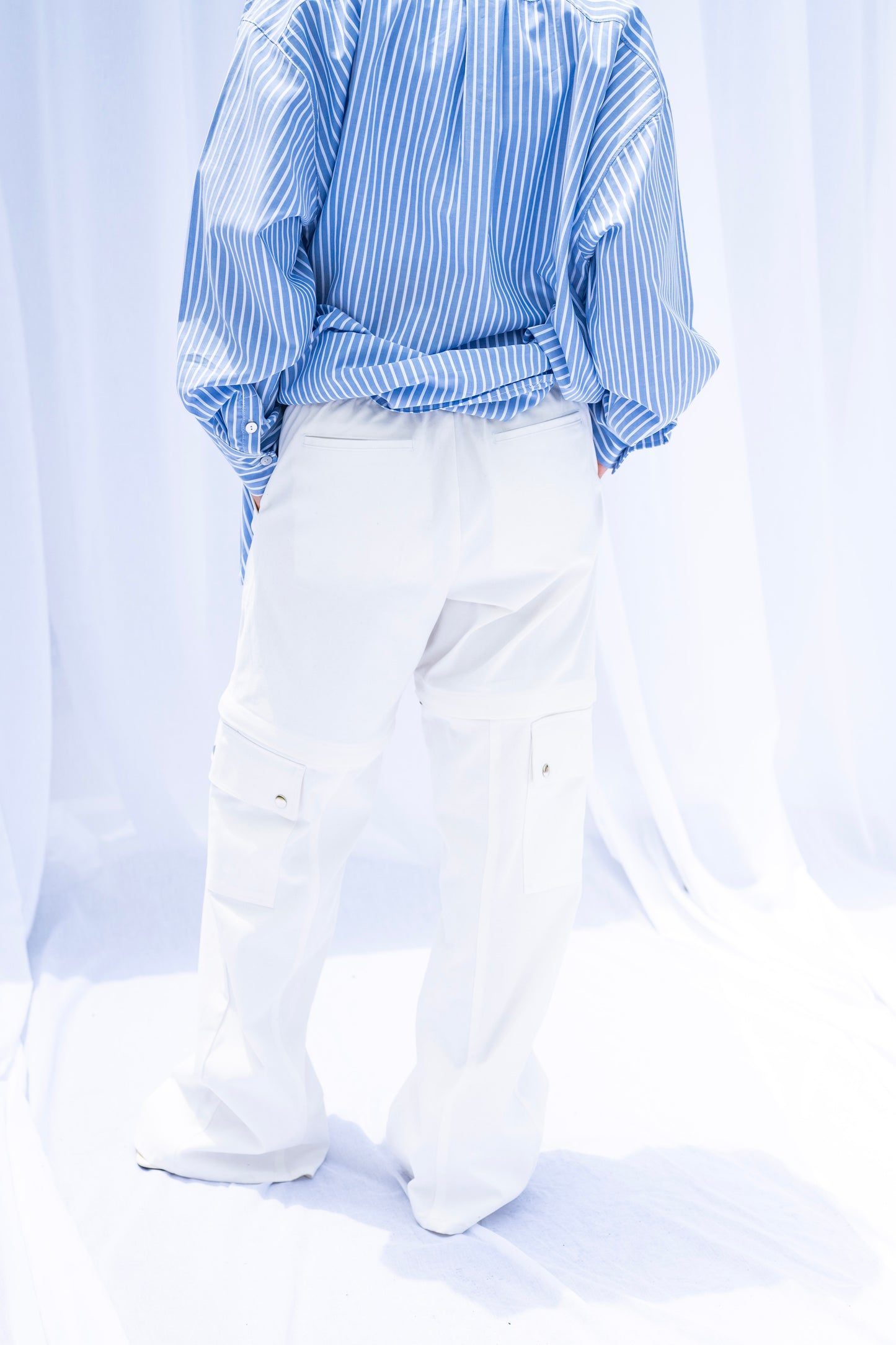 Person wearing a blue and white striped shirt with white pants on a light gray background