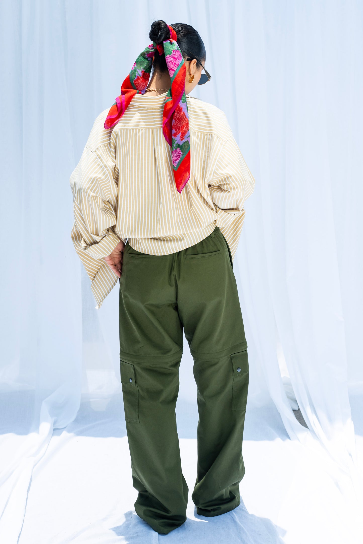 Person wearing a beige shirt, green pants, and a colorful scarf on a white background