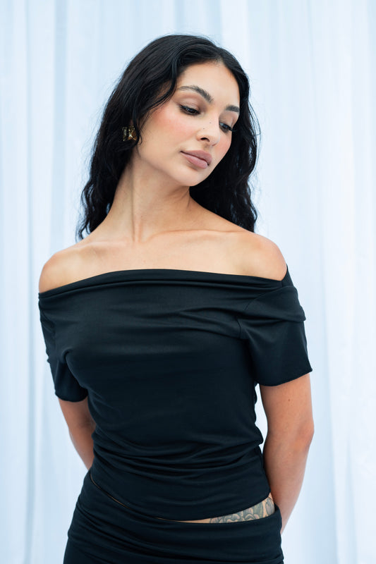 Woman wearing a black off-shoulder top against a white curtain background
