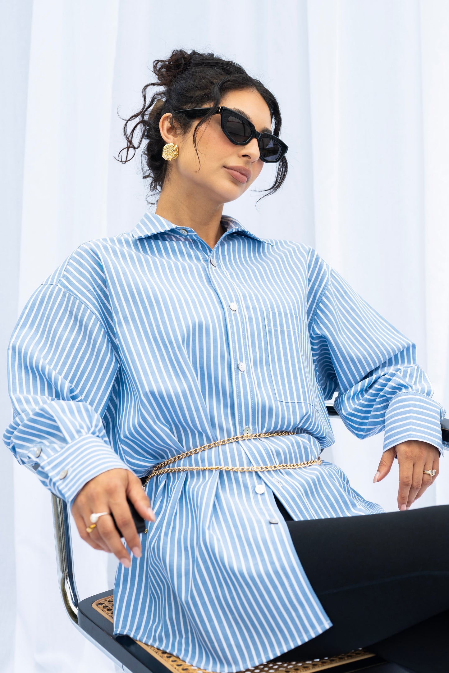 Woman wearing a blue and white striped shirt with a belt, sitting on a chair.