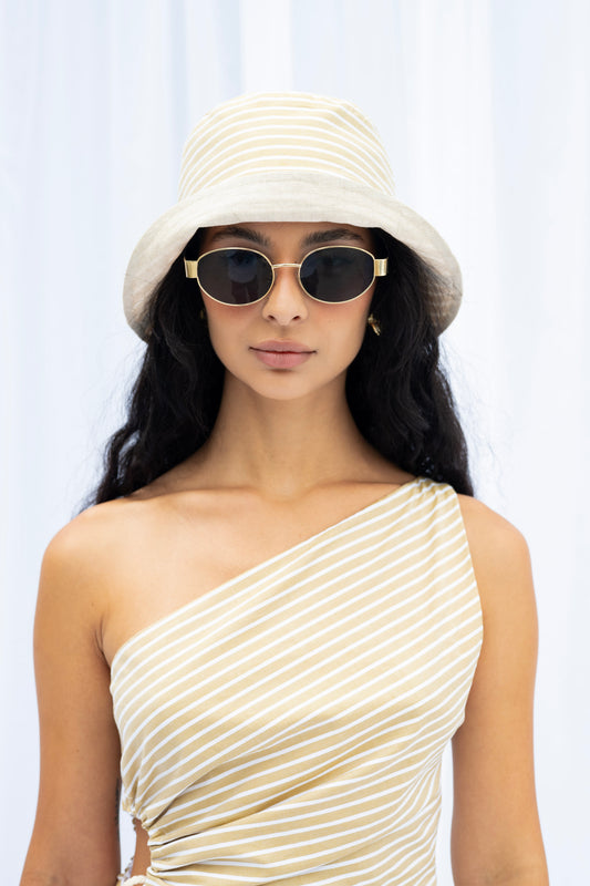 Woman wearing a white bucket hat and one-shoulder dress against a light background