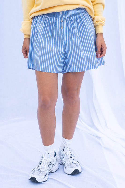 Person wearing blue and white striped shorts with a yellow top on a light gray background