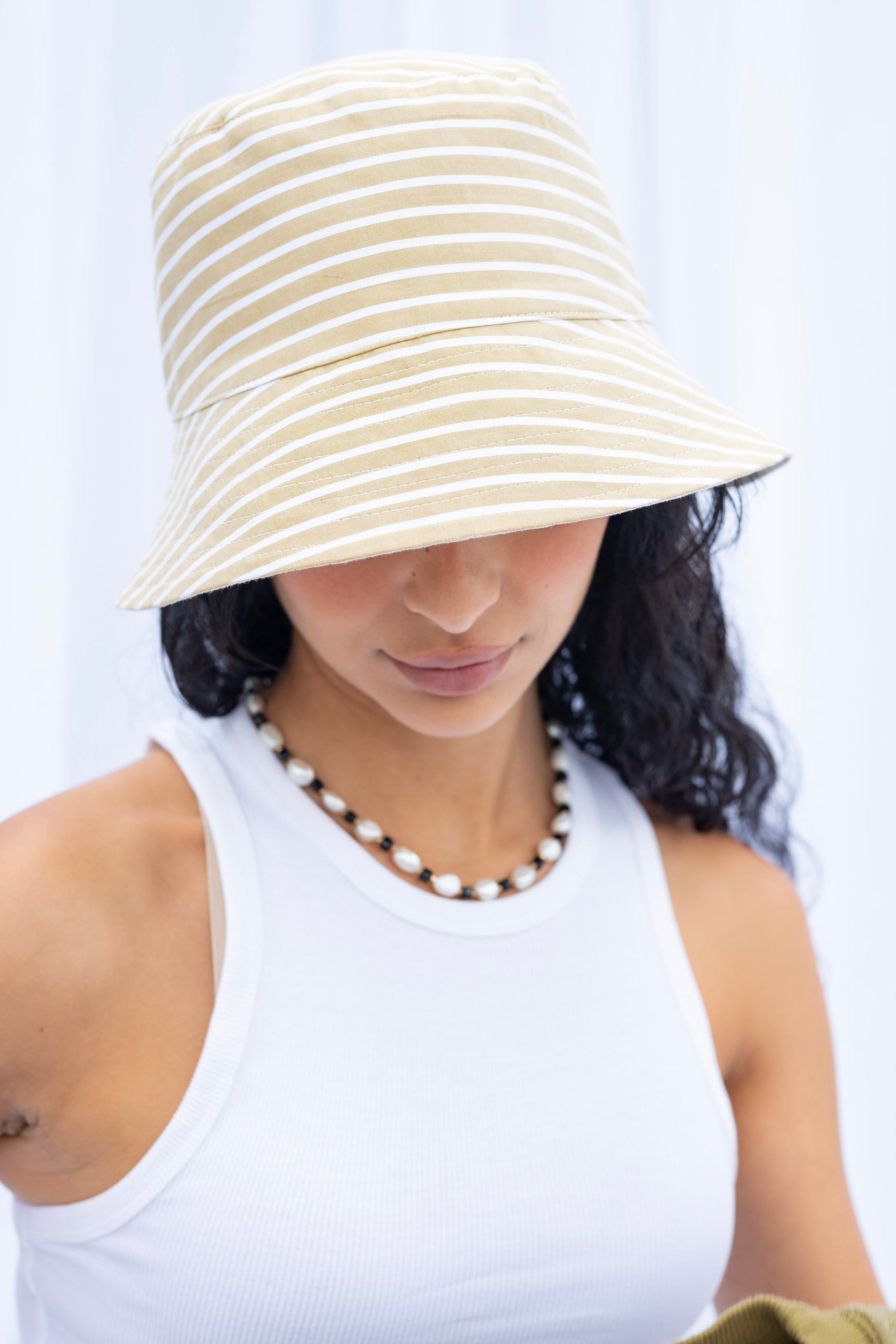 Woman wearing a beige and white striped bucket hat against a white background