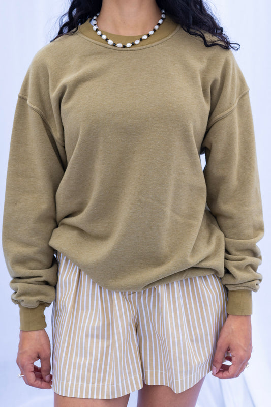 Person wearing a beige sweatshirt and striped shorts on a white background