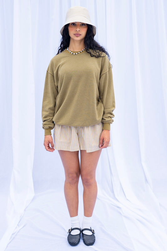 Woman wearing a green sweater, beige shorts, and a white bucket hat on a white background
