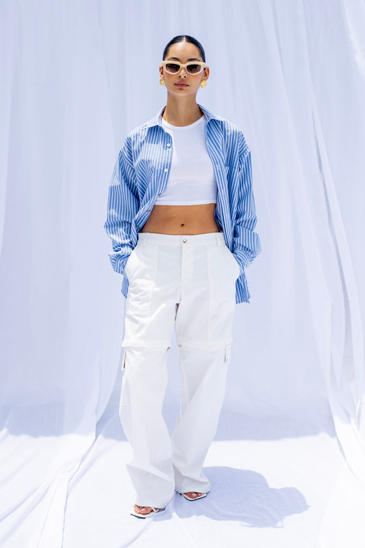 Person wearing a blue and white checkered shirt, white pants, and sunglasses on a white background