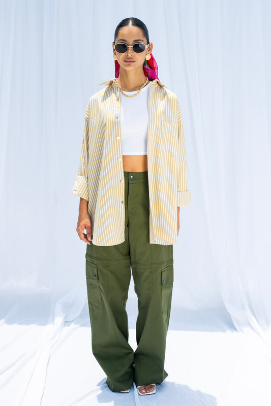 Person wearing a beige shirt, white crop top, green pants, and sunglasses on a light blue background