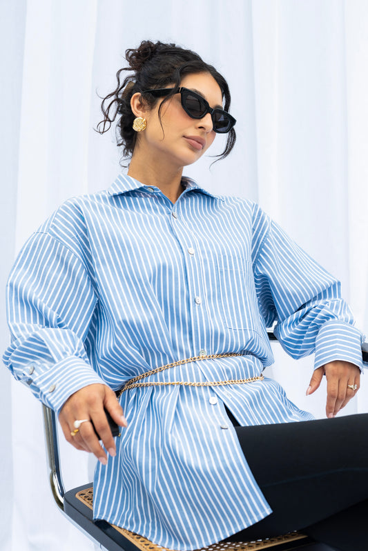 Woman wearing a blue and white striped shirt with a belt, sitting on a chair.