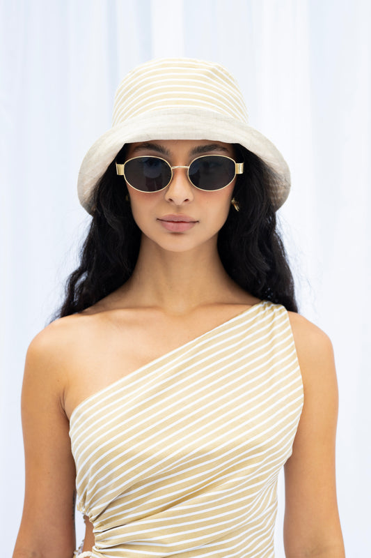 Woman wearing a white bucket hat and one-shoulder dress against a light background